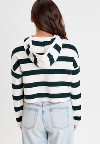 Haut à capuche coupé avec des rayures horizontales vertes et blanches, doté d'une capuche et d'un tissu doux, associé à un jean taille haute bleu clair.