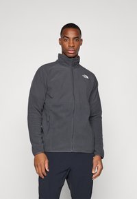 Ciemnoszara polarowa kurtka z wysokim kołnierzem, zamkiem z przodu, kontrastowymi teksturowanymi panelami oraz logo The North Face na górze po lewej stronie.