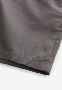 Harmaat kangashousut, joissa on sileä pinta, suora helma ja hienovaraisia ompelutuksia. Materiaali vaikuttaa kevyeltä ja hengittävältä.