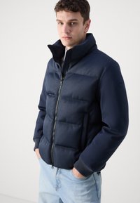 Μπουφάν ναυτικού τύπου με υφή σε ρίγες στο επάνω μισό, λείες μανσέτες, ψηλό γιακά και μπροστινό φερμουάρ. Διαθέτει ελαστικές μανσέτες και μέση.