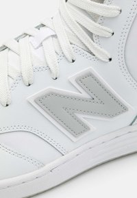 White sneaker with a smooth leather upper, featuring a prominent grey "N" logo, flat white laces, and a textured rubber sole.