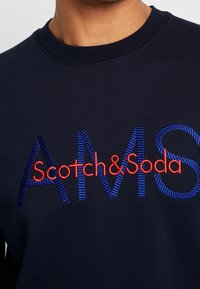 Sudadera de la marina con el logo "Scotch&Soda" bordado en rojo y azul. Diseño de cuello redondo con textura acanalada.