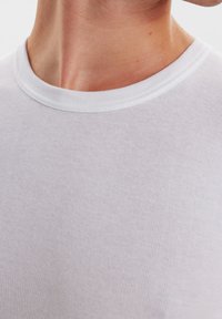 Hvid bomulds T-shirt med ribbet tekstur, rund halsudskæring og tætsiddende design. Synlig syning omkring kraven.
