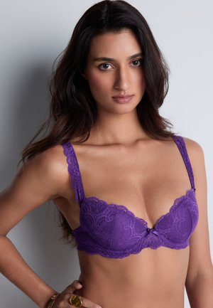 Soutien-gorge en dentelle violette avec des bords en feston, soutien-gorge à armatures et un accent en nœud à l'avant. Le tissu présente un motif floral et des bretelles réglables.