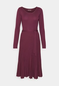 Robe à manches longues de couleur bordeaux foncé, avec un corsage ajusté et une jupe plissée, accompagnée d'une ceinture en tissu attachée à la taille.