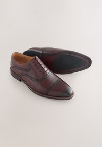 Chaussures habillées en cuir bordeaux avec bout foncé et détails brogues. Fermeture à lacets, intérieur marron et semelle en caoutchouc antidérapante.