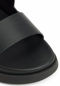 Sandale noire à glissière avec une large bride texturée et une pointe ronde lisse. La semelle intérieure est rembourrée avec une semelle extérieure basse et ferme.