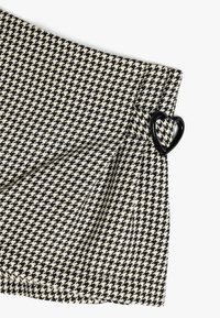 Stoff mit Hahnentritt-Muster in Schwarz und Weiß mit gefaltetem Design. Verfügt über eine schwarze herzförmige Schnallenakzent. Maßgeschneiderte und strukturierte Oberfläche.