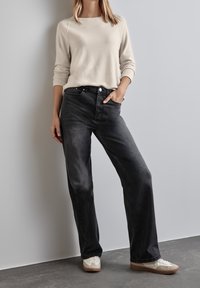 Jasnobeżowy sweter w połączeniu z luźnymi, wyblakłymi czarnymi dżinsami. Białe sneakersy z beżowymi akcentami. Prosty, klasyczny design z minimalną ilością detali.