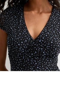 Černé květované šaty s malými modrými květy, s krátkými rukávy a hlubokým výstřihem do V. Mají dekorativní mašli u výstřihu a strukturovanou látku.
