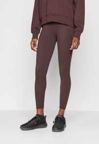 Barna leggings sima textúrával és testhez simul�ó fazonnal, egy hozzá illő oversized pulóverrel és fekete sportcipővel párosítva.
