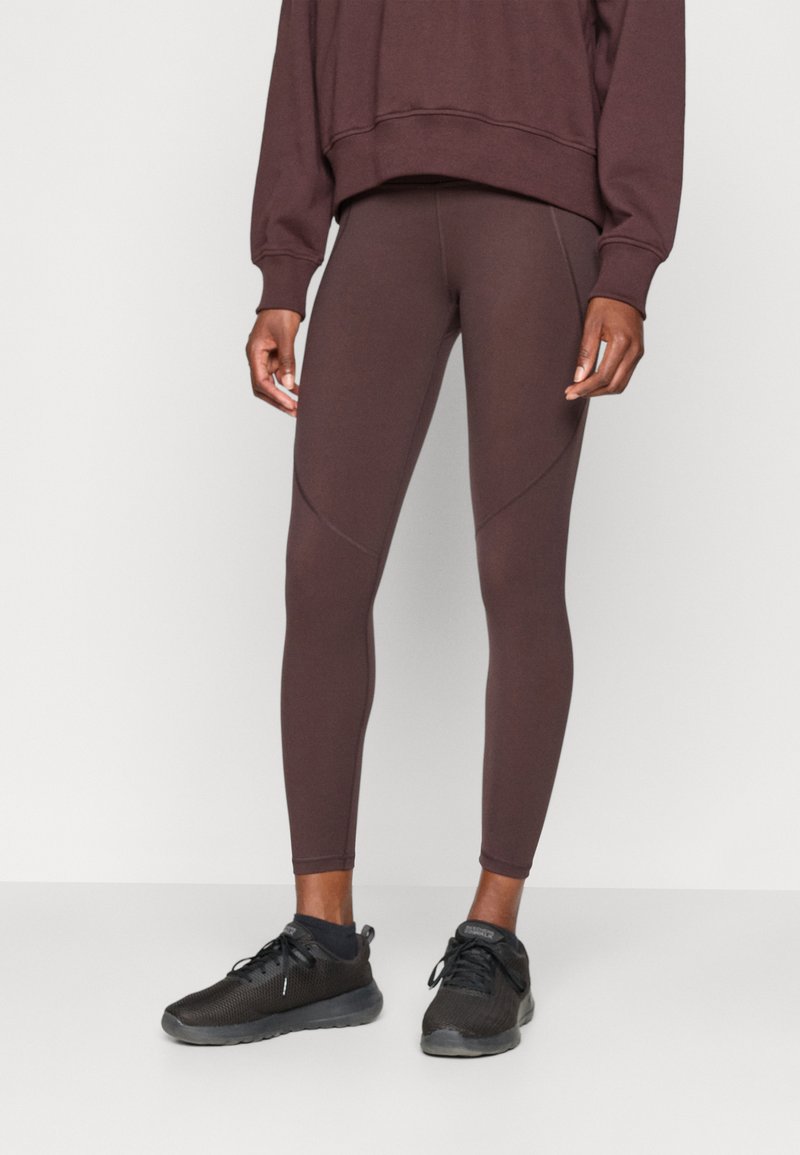 Barna leggings sima textúrával és testhez simuló fazonnal, egy hozzá illő oversized pulóverrel és fekete sportcipővel párosítva.