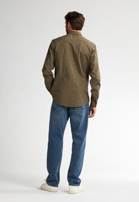 Camisa verde con estampado, de manga larga y cuello abotonado; combinada con vaqueros de corte relajado en azul y zapatillas blancas.
