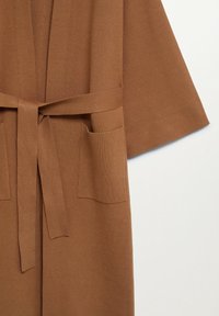 Cardigan marron en tricot avec des manches larges, deux poches avant et une ceinture assortie nouée au centre.