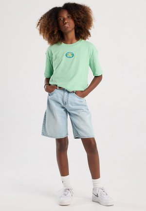 Camiseta de manga corta verde menta con un gráfico circular; pantalones cortos de mezclilla azul claro; zapatillas blancas; calcetines texturizados. Conjunto casual mostrado.