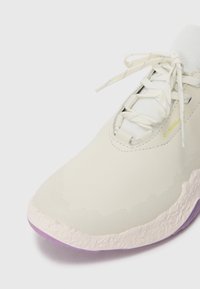 Lättvikts, gräddfärgad sneaker med en slät, texturerad ovandel, lila sula och snörning med en vadderad mellanläst.
