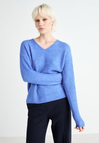 Lyseblå, ribbestrikket genser med V-hals og lange ermer, kombinert med mørke bukser. Teksturen ser myk og koselig ut.