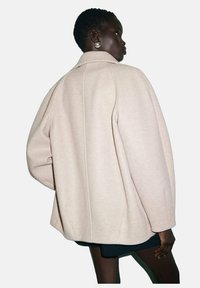 Cappotto oversize in misto lana beige con silhouette strutturata, ampio colletto e dettagli di cucitura sottili. Presenta maniche rilassate e larghe.