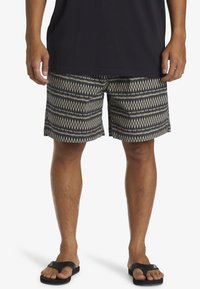Svarta shorts med vita diamant- och pilmönster, tillverkade av lätt tyg, har en rak skärning och en slät textur. Bärs medtofflor.