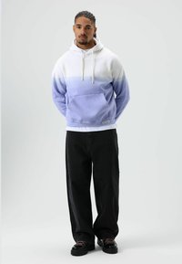 Kapuzensweatshirt in Weiß-Lavendel-Verlauf, mit Fronttasche und Kordelzug. Kombiniert mit lockeren schwarzen Hosen und klobigen schwarzen Schuhen.