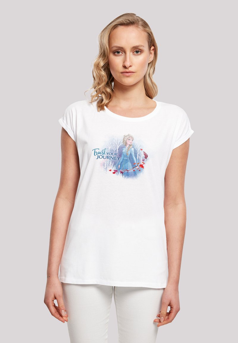Hvid t-shirt med korte ærmer, der har et design af en karakter i en blå kjole, omkranset af træer og teksten "Stol på din rejse."