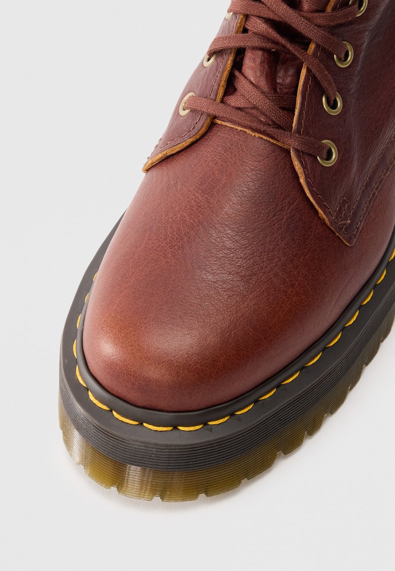 Bottines en cuir marron avec un bout rond, une épaisse semelle transparente, des surpiqûres jaunes le long du bord et des œillets en métal pour les lacets.