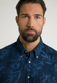 Donkerblauwe overhemd met knoopsluiting van stof met een bloemenpatroon in een lichtere blauwe tint. Inclusief een borstzak en een klassieke kraag.