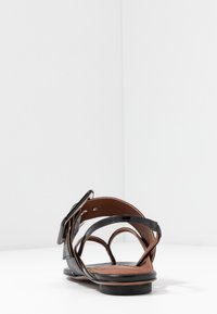 Sandal con tacco nero e multiple cinghie con fibbia, con una texture liscia e una soletta marrone, su uno sfondo bianco.