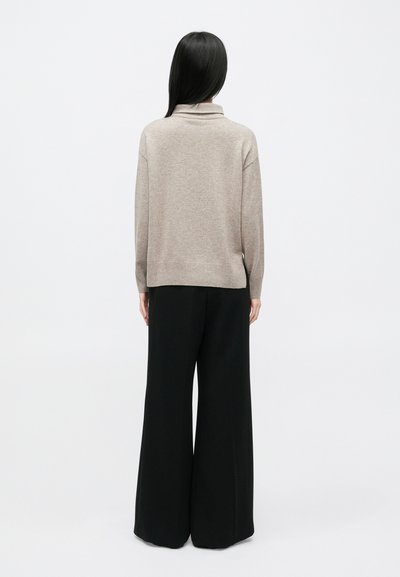 Μπεζ πλεκτό πουλόβερ με ψηλό γιακά, φορεμένο με μαύρο παντελόνι φαρδιάς γραμμής. Ομαλή υφή και άνετη εφαρμογή αποτελούν χαρακτηριστικά του.
