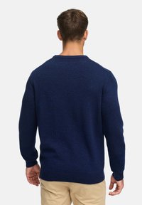 Marineblå strikket genser med rund hals og ribbestrikkede mansjetter. Myk tekstur, klassisk passform, og minimalistisk design uten synlige logoer.