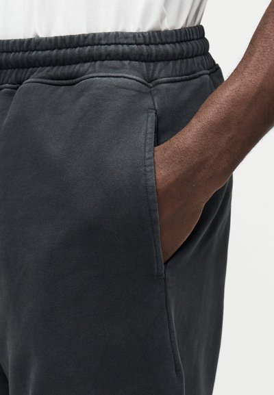 Sötétszürke, puha anyagból készült melegítőnadrág, elasztikus derékrésszel és oldalzsebekkel. Látható varrási részletekkel rendelkezik.