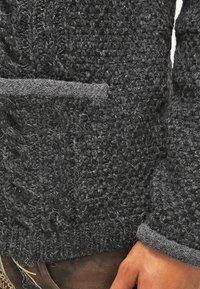 Gestructureerde donkergrijze gebreide trui met een zachte, pluizige afwerking, voorzien van een opvallende zak en gedefinieerde geribbelde manchetten.