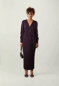 Lilla kootud kleit V-kaelusega, pikkade varrukatega ja vööga. Omab ribatekstuuri ja lõtvunud serva. Mudel hoiab käes väikest kotti.