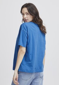Camiseta de algodón azul con un corte relajado, mangas cortas y ligeras variaciones en la textura; combinada con jeans de mezclilla de lavado claro.