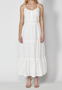 Vit maxiklänning med blommigt ögonlappsmönster, tunna axelband, knäppning framtill, lager-på-lager volangkant och lätt bomullstyg.