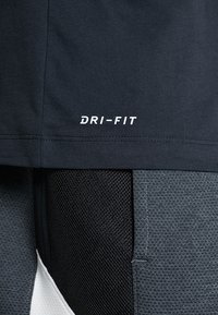 Top deportivo Dri-FIT negro con textura suave y logo blanco. Combinado con pantalones cortos grises con textura que presentan paneles de malla y detalles de costura.