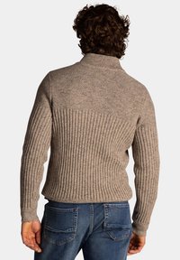 Beige geribbelde trui met hoge kraag en gestructureerd breiwerk. De onderkant heeft verticale strepen, die aansluiten bij het gladde bovenste gedeelte.