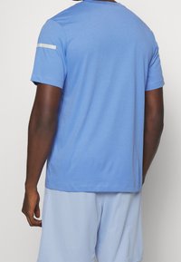 Camisa de manga corta azul claro con cuello redondo, que presenta una franja blanca horizontal en el hombro y una textura suave de algodón.