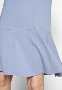 Valkoinen sininen mekko, jossa on liehuva helma, valmistettu pehmeästä puuvillamateriaalista. Siinä on sauma flounce-yllä ja sileä pinta koko matkalla.