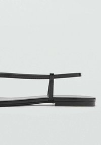 Mustat litteät sandaalit ohuilla hihnoilla, minimalistinen muotoilu, sileä pinta ja matala pohja, sopii arkikäyttöön.