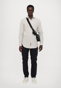 Checkered shirt in light gray, black strap bag across the body, dark pants, and white sneakers. Simple design with button details.