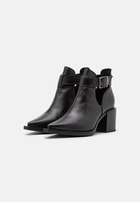 Schwarze Knöchelstiefel aus glattem Leder, mit spitzer Zehenform, Blockabsatz und einem verstellbaren Riemen mit einer silbernen Schnalle.