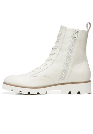 White leather ankle boots with a textured finish, featuring a front lace-up design and a side zipper. Thick white rubber sole with a tan edge.