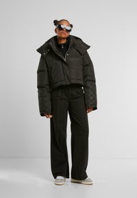 Sort cropped dunjakke med oversized ærmer, sølv hardware og broderet logo. Kombineret med vidde ben sorte bukser og grå sneakers.