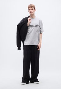 Γκρι κοντομάνικο μπλουζάκι με οριζόντιες μαύρες ρίγες, συνδυασμένο με φαρδιά μαύρη παντελόνα. Το μοντέλο κρατάει ένα μαύρο σακάκι πάνω σε έναν ώμο.