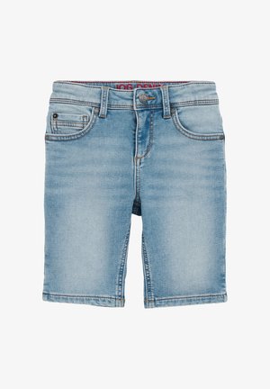 Barn iført en grøn T-shirt med korte ærmer og palmeprint, lyseblå op-rullede denimshorts og beige sneakers med hvide snørebånd.