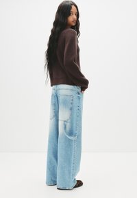 Maglione marrone a maglia abbinato a jeans in denim a gamba larga di colore blu chiaro. I jeans hanno grandi tasche posteriori e un lavaggio sbiadito.