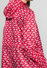 Czerwona kurtka puchowa z powtarzającym się wzorem białych psów. Z kapturem, o gładkiej, błyszczącej fakturze i elastycznych detalach przy mankietach.