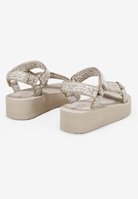 Sandalias de plataforma beige con correas de tejido texturizado y cierres de hebilla ajustables. Suela plana con acabado en un tono marrón claro similar a la madera.