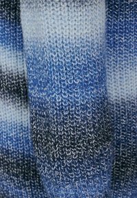 Stickad plagg med en gradientmönster i olika blå nyanser, från ljus till mörk, med en strukturerad väv och lösa, mjuka fibrer.